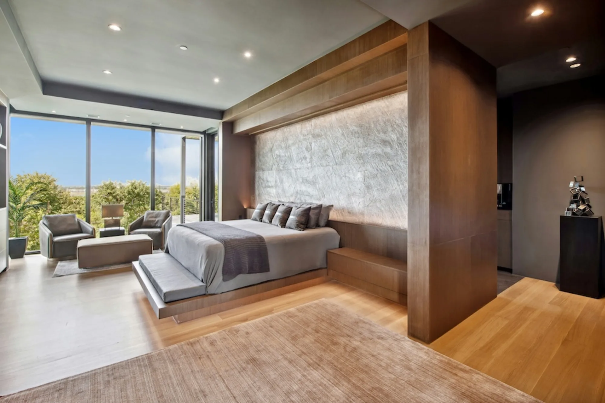 A large, sunlit bedroom with floor-to-ceiling windows and a rumpled bed